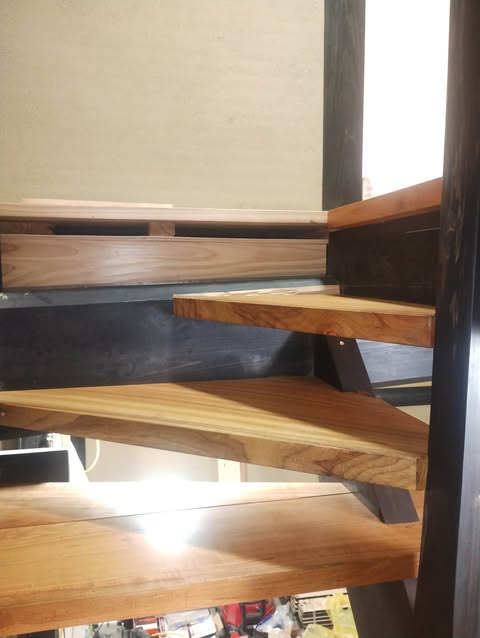 649563631_1489554002507294_1758967348663322930_n - NO1製材機ウッドマイザー正規販売代理店│ウッドマイザージャパン MSco.,LTD. Close-up of a wooden staircase with thick treads, open risers, and dark metal stringers against a light wall.