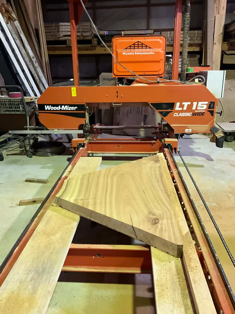 image - NO1製材機ウッドマイザー正規販売代理店│ウッドマイザージャパン MSco.,LTD. Orange Wood-Mizer LT15 Classic Wide bandsaw in a wood shop, with a thick wooden board across the saw bed ready to cut