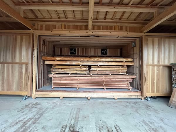 Stacks of wooden planks and beams stored in a carpentry shop shed or storage bay.