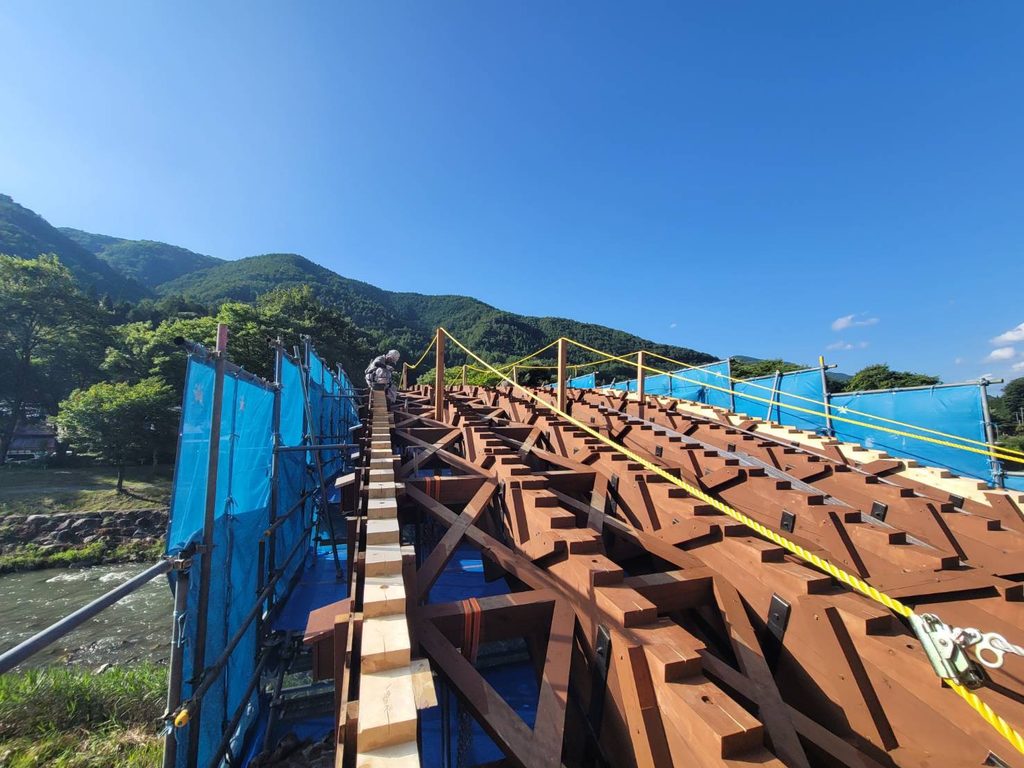 床板が外されトラス構造と足場がむき出しになった木造アーチ橋の解体・修復工事風景